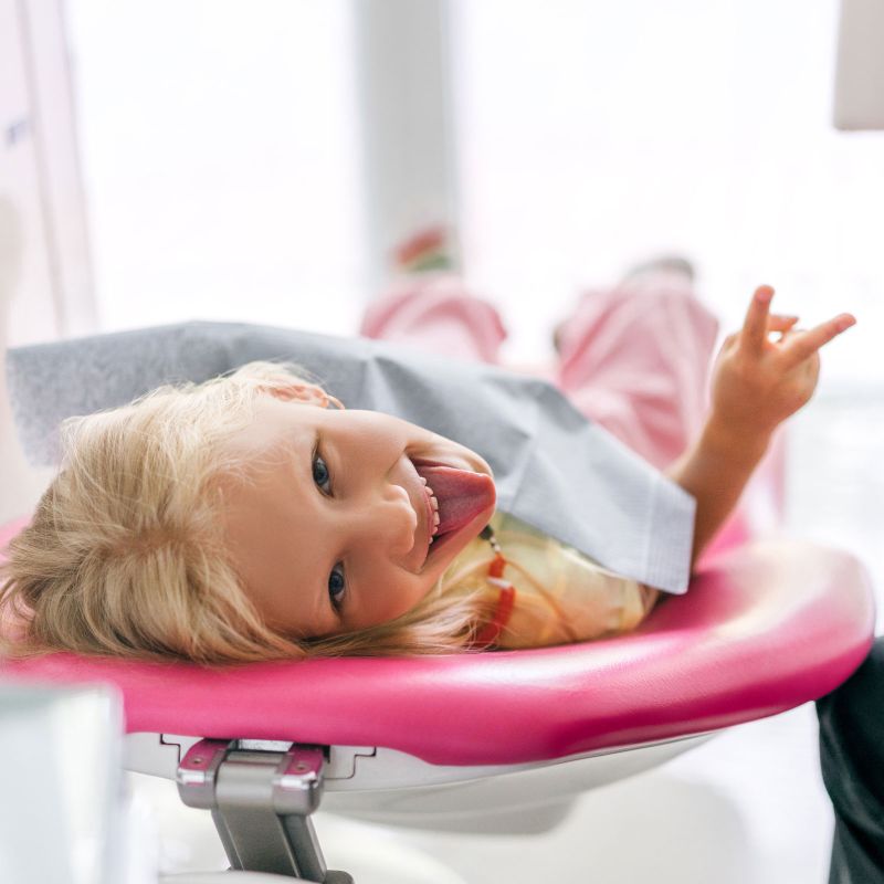 Kind liegt auf einem pinken Behandlungsstuhl und streckt die Zunge heraus.